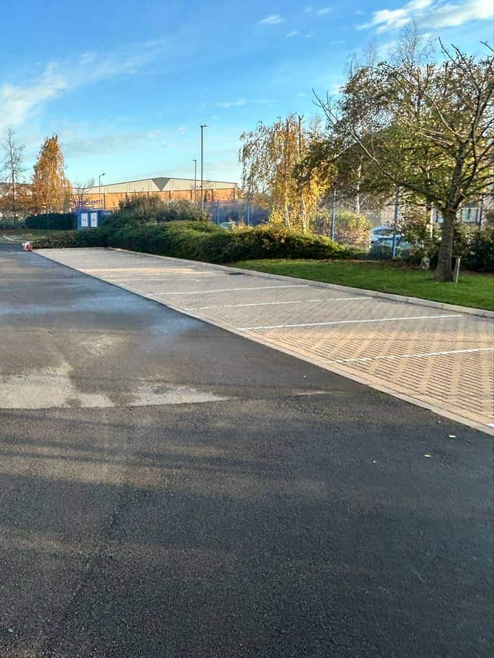 Clean buff block-paved parking bays beside a wet tarmac access road under a blue sky