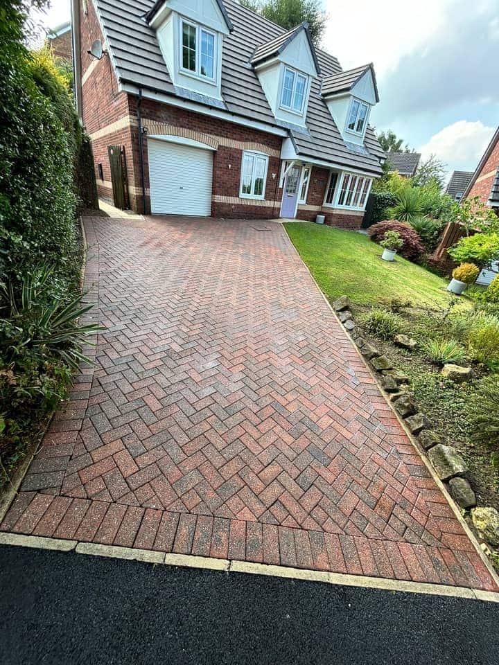 The same driveway after cleaning, red and charcoal herringbone blocks running up to the garage