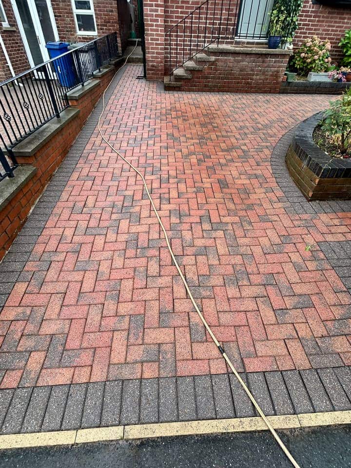 Bright red herringbone block paving with a charcoal border after cleaning, steps and a planter behind