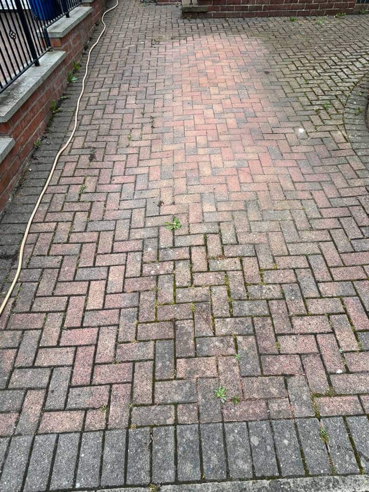 Faded block paving with dark joints beside black railings, a hose lying across it