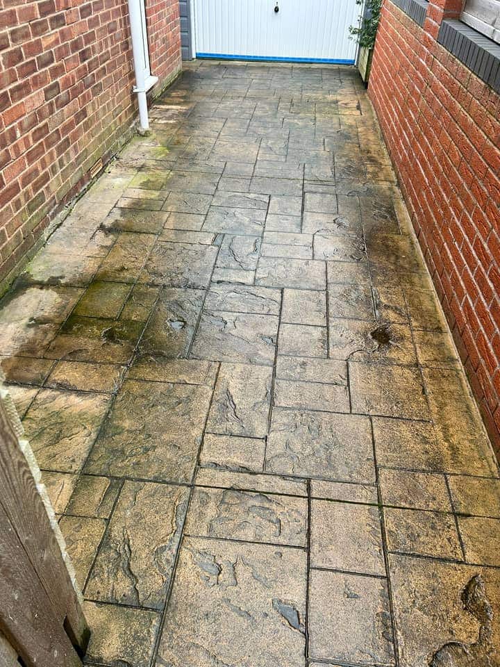 Narrow imprinted concrete driveway stained green and black along a brick wall
