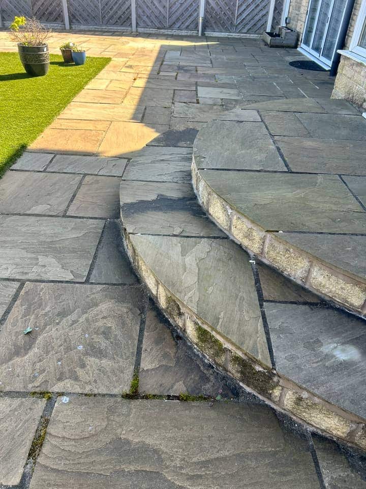 Grey weathered stone patio with two curved steps, dark staining on the risers