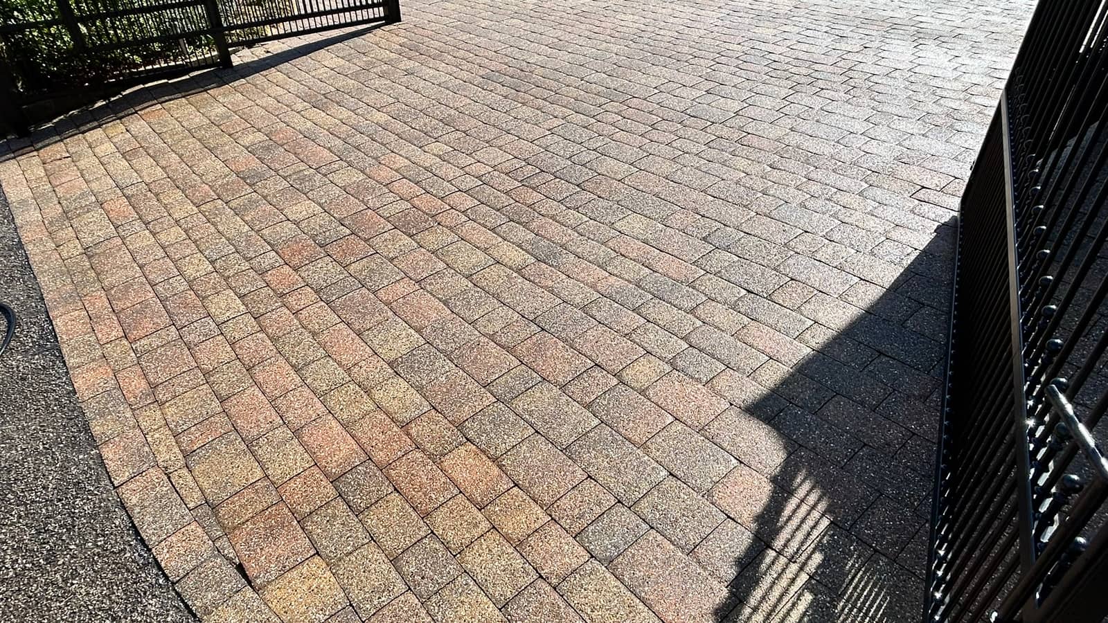 A cleaned brindle block-paved driveway in low sun, the shadow of iron gates falling across it