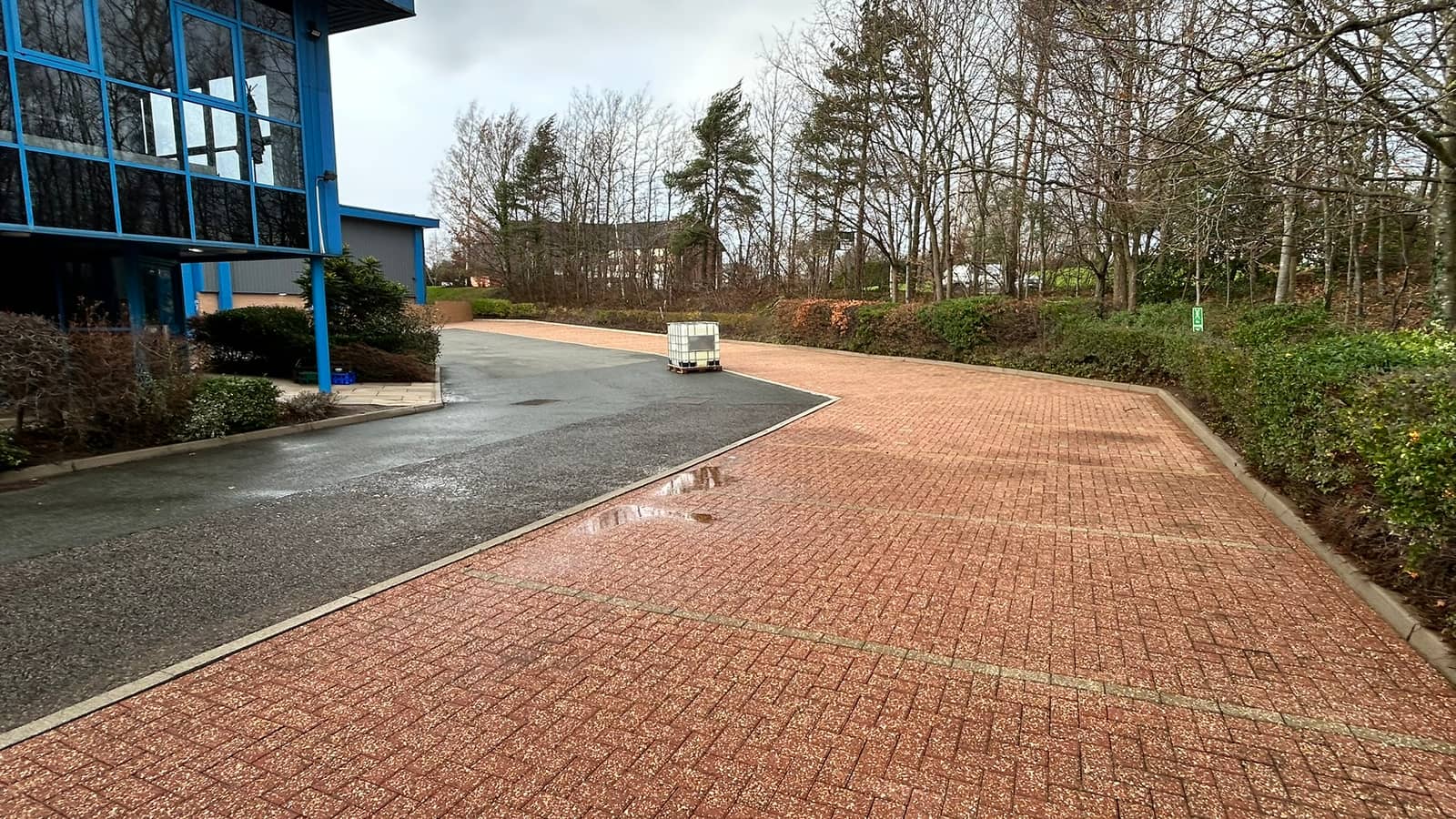 A cleaned red block-paved car park curving past a blue glazed office building