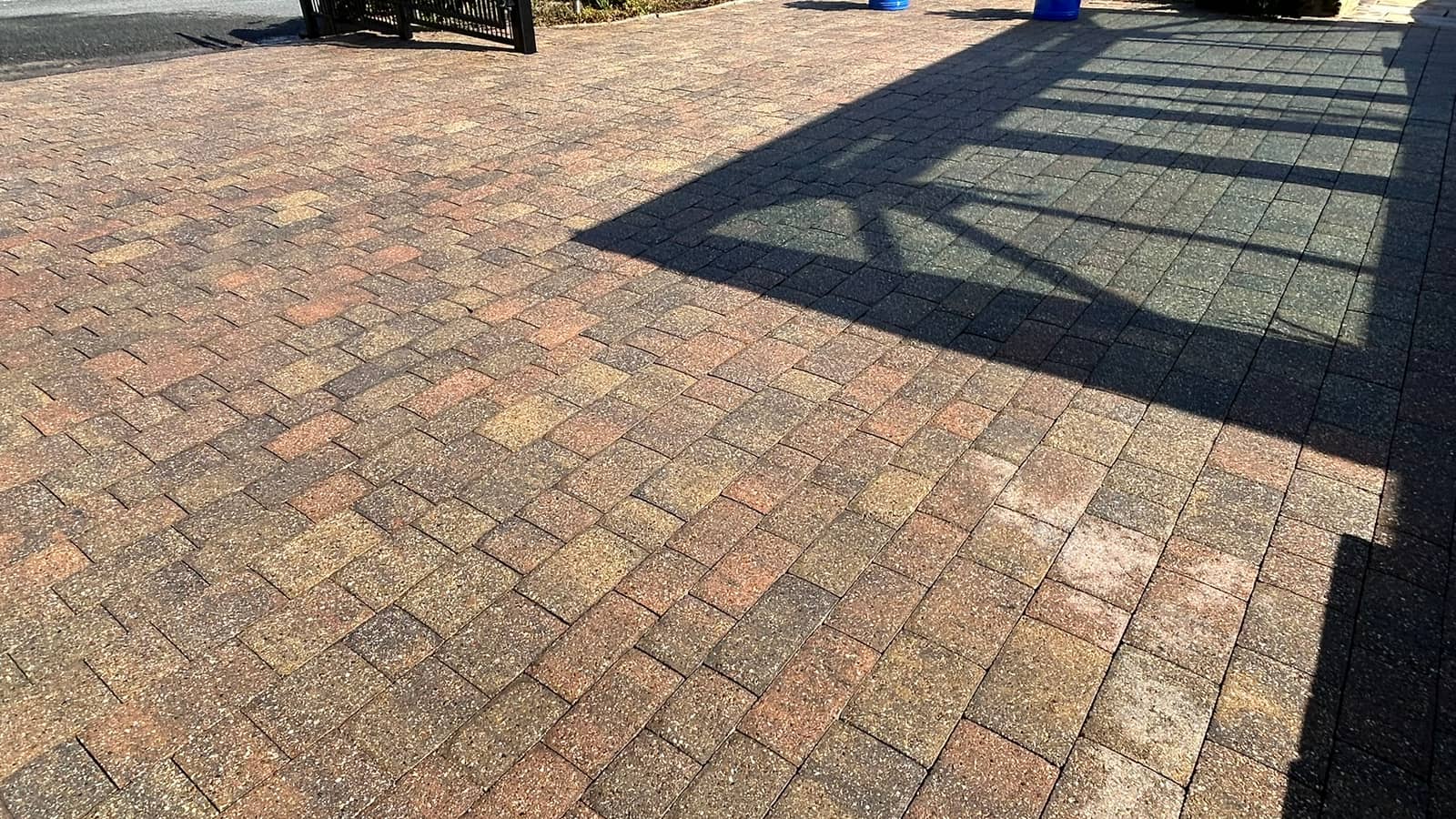 A cleaned brindle block-paved driveway with the shadow of railings across one corner
