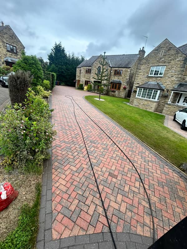 Long red herringbone drive leading to a stone house, after cleaning