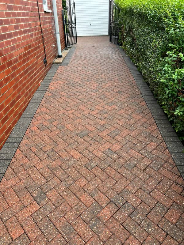 Red block-paved side drive running to a white garage door, after cleaning
