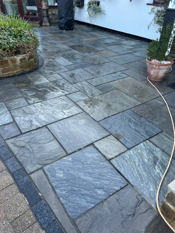 Dark grey stone patio, wet and clean, beside a white rendered wall