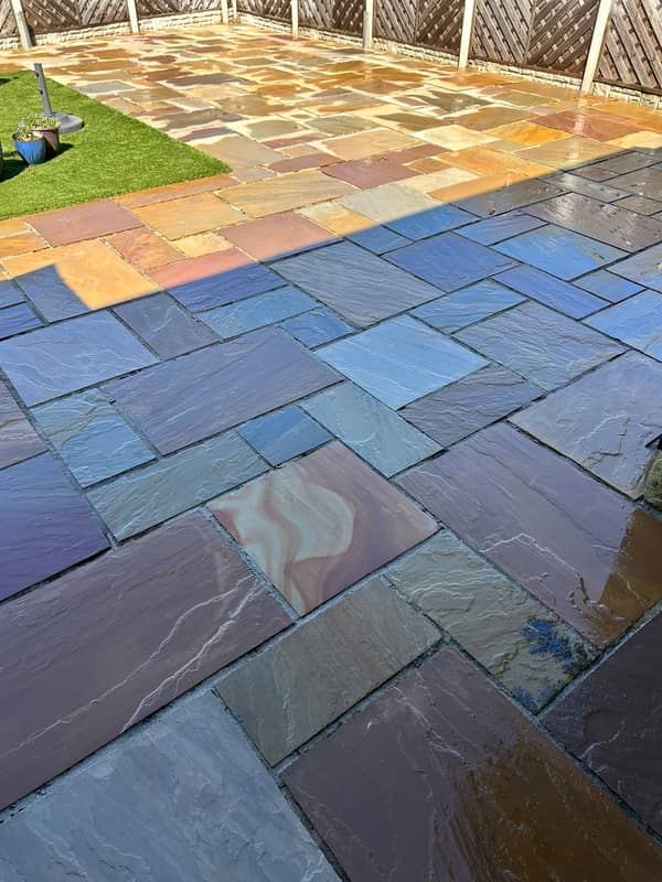 Multi-coloured Indian stone patio, wet after cleaning, with a lattice fence behind