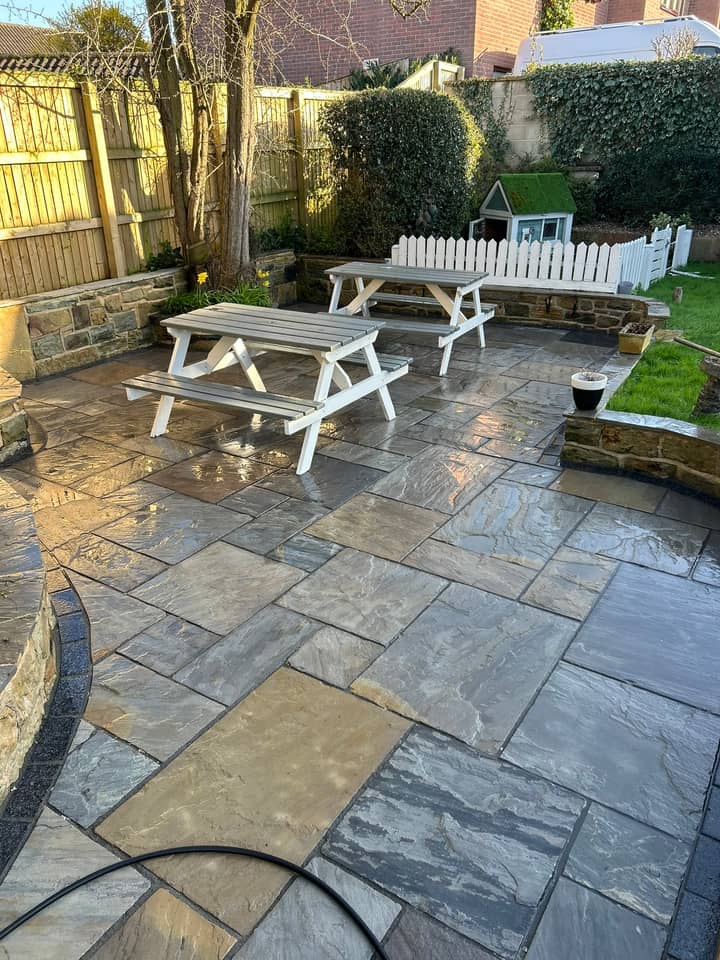 A cleaned stone patio with white picnic benches and a small playhouse behind