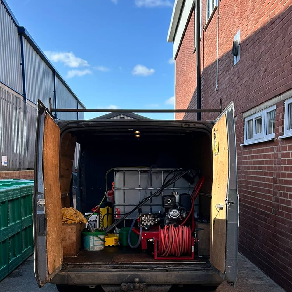 The back of the work van with its doors open, showing a water tank, a petrol-driven pump and a red hose reel