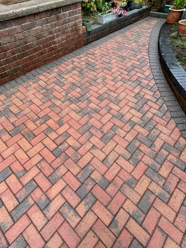 A cleaned red and charcoal herringbone block-paved path curving beside a raised brick bed