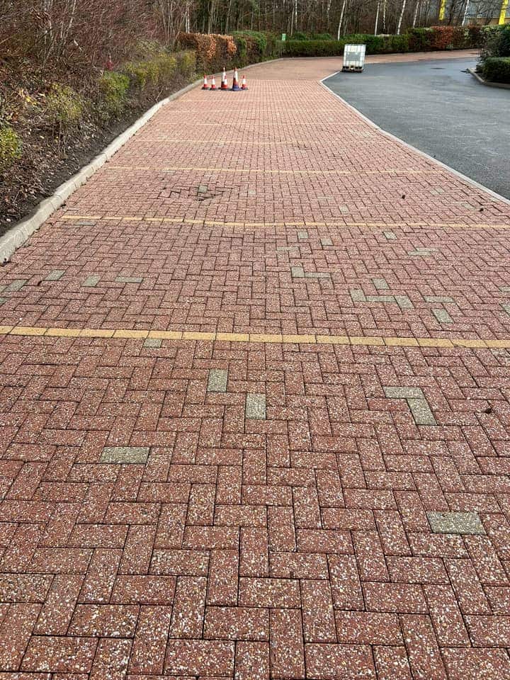 A long run of red block-paved parking bays after cleaning, with yellow bay lines and cones at the far end