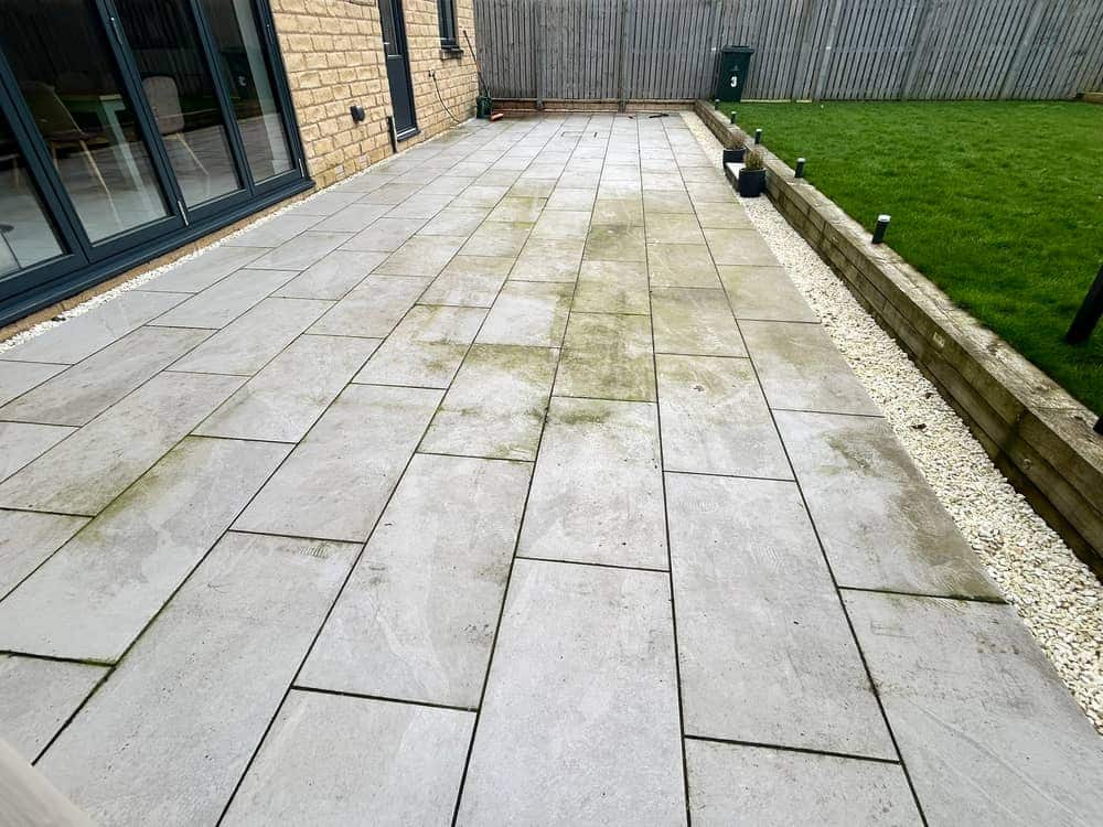 Long pale porcelain patio with green streaks across the slabs, beside bifold doors