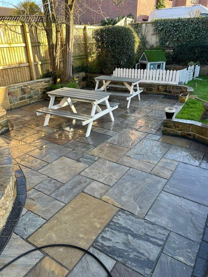 The same patio after cleaning, grey and buff stone slabs wet and clean around white picnic benches
