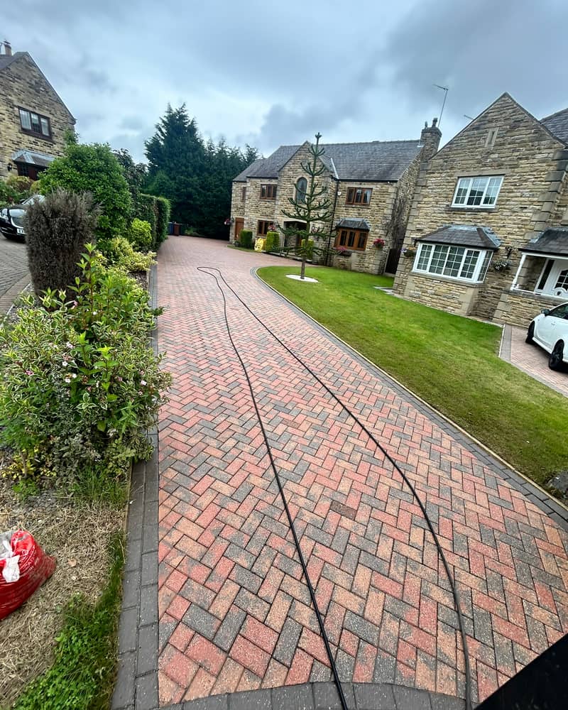 A long red herringbone block-paved drive, freshly cleaned, sweeping up to a large stone house